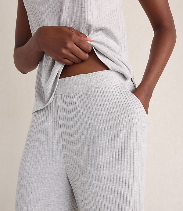 A person wearing a light grey ribbed lounge set stands against a neutral, textured beige background.