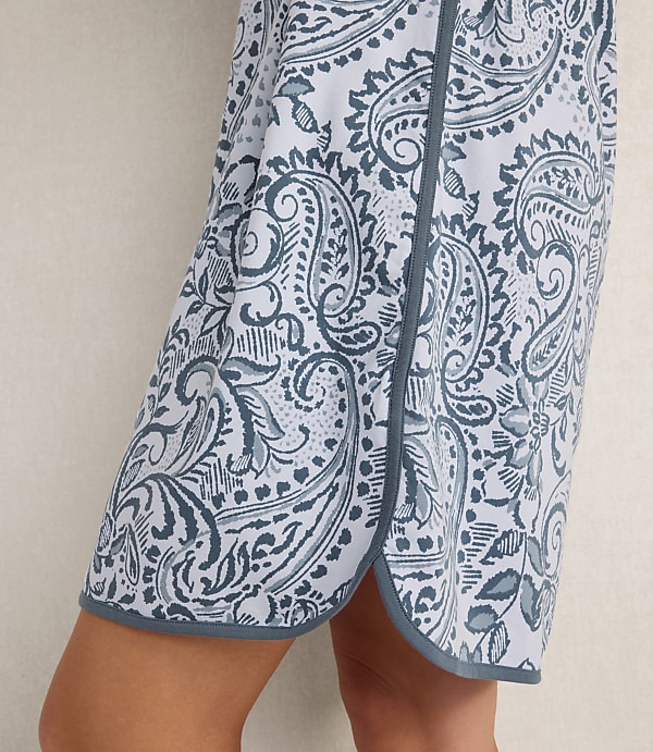 A person wears a blue and white paisley print skirt against a plain, light-colored background.
