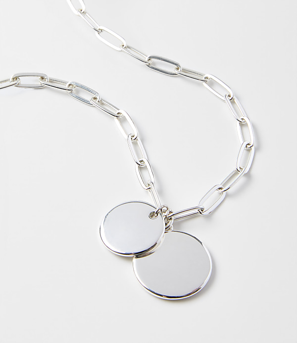 A silver chain necklace with two circular pendants rests on a plain white background.