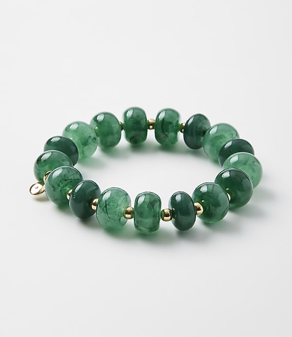 A bracelet of polished green stone beads with small gold spacers rests on a plain white background.
