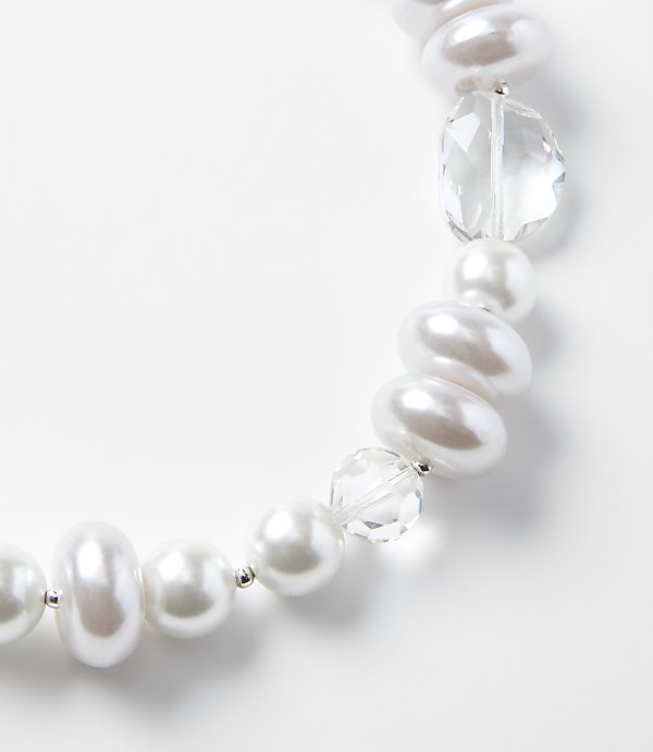 A string of white pearls and clear faceted crystals curves across a plain white background.