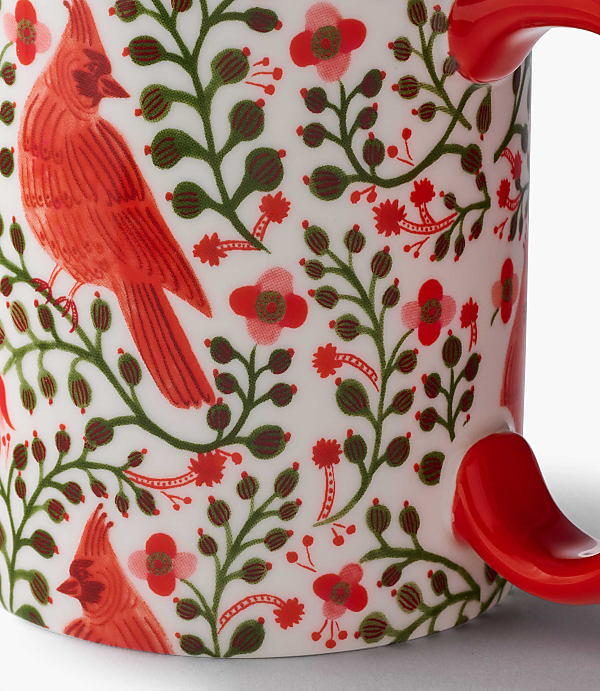 A white mug features a pattern of red cardinals and green foliage against a plain white background.