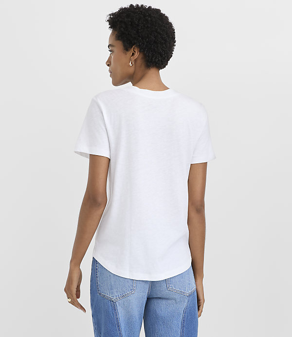 A woman wearing a white t-shirt and blue jeans stands with her back to the camera against a plain white background.
