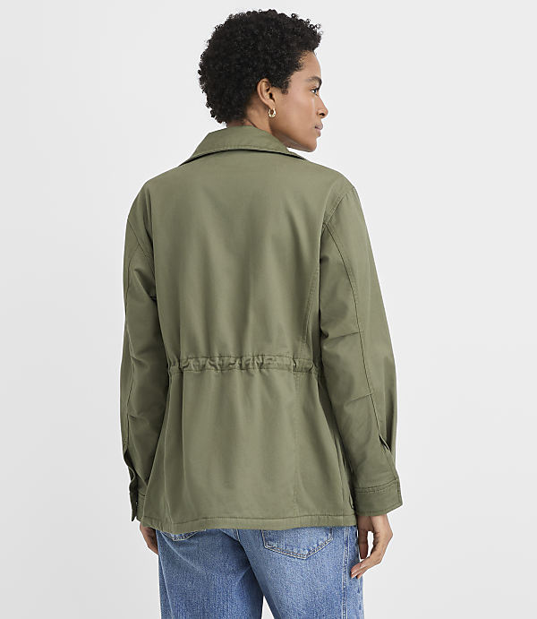 A woman in a green jacket and denim skirt stands against a plain white background.