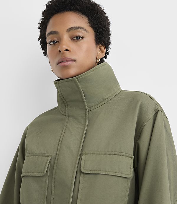 A woman with short curly hair wearing an olive green high-collar jacket poses against a plain white background.