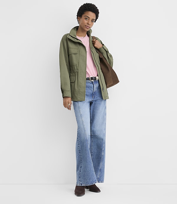 A woman in a green jacket and denim skirt stands against a plain white background.