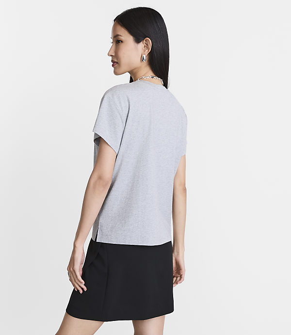 A woman in a grey t-shirt and black skirt stands against a plain white background.