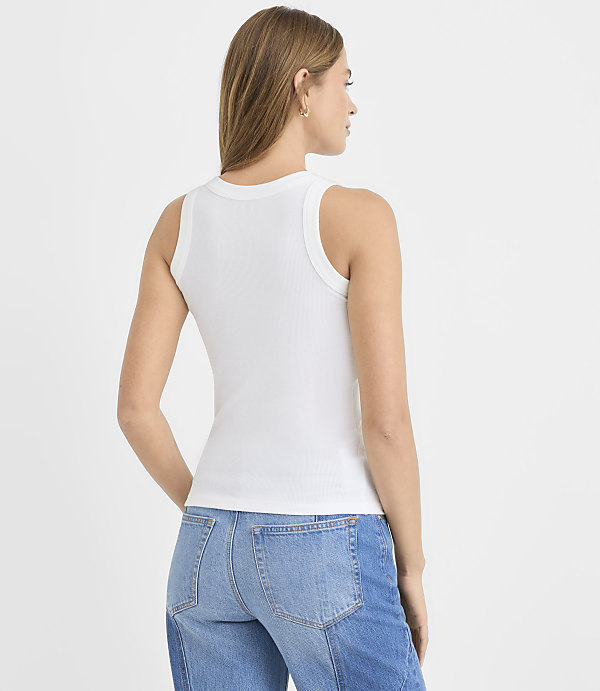 A woman wearing a white ribbed tank top and blue jeans stands with her back to the camera against a plain white background.