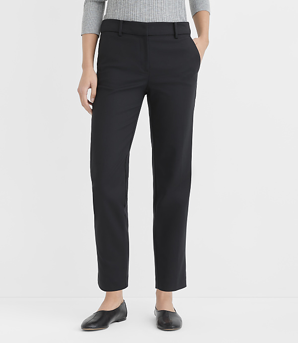 A person stands in black pants and flats against a plain white background.