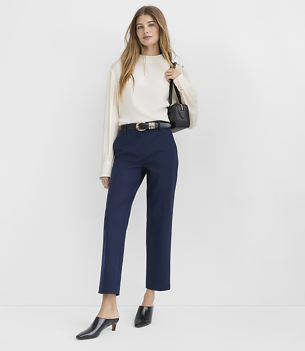 A woman in a denim jacket, patterned top, and navy pants stands against a plain white background.