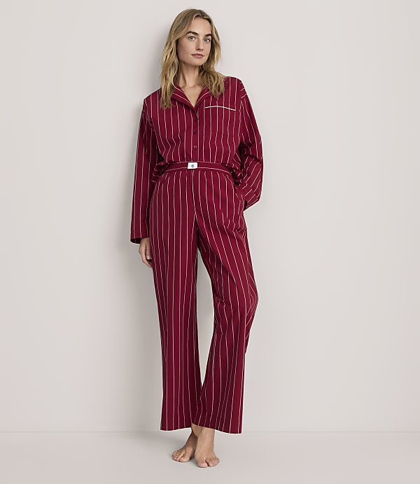 A woman wearing red striped pajamas stands against a plain, light-colored background.
